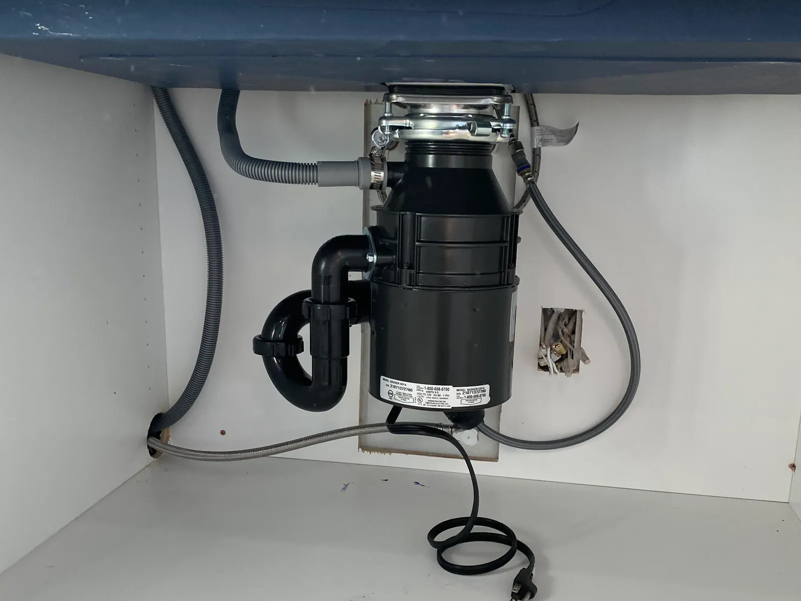 Garbage disposal installed under a kitchen sink, with its drain and hoses connected