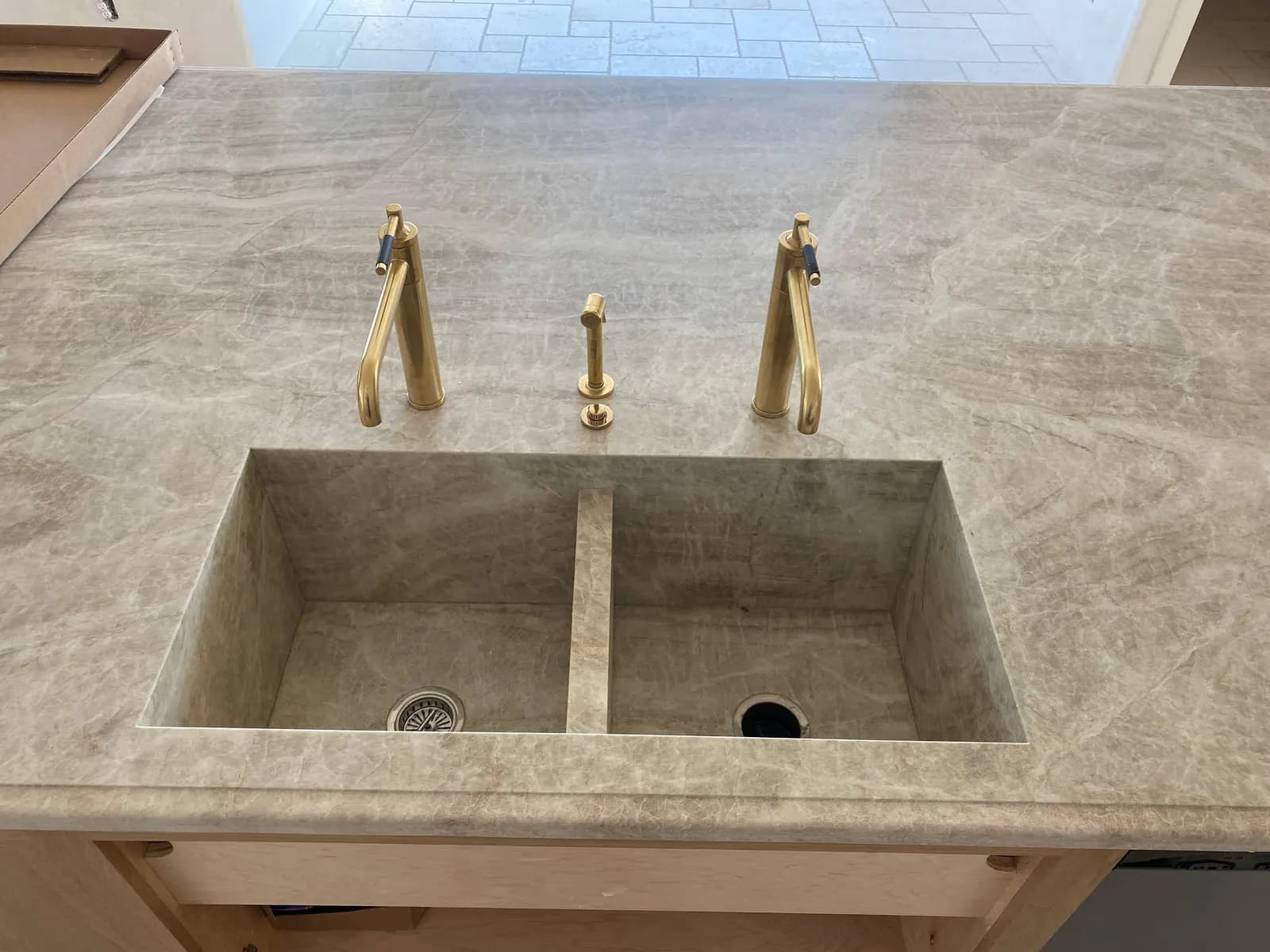 Brass faucets installed on a double stone sink in a kitchen island